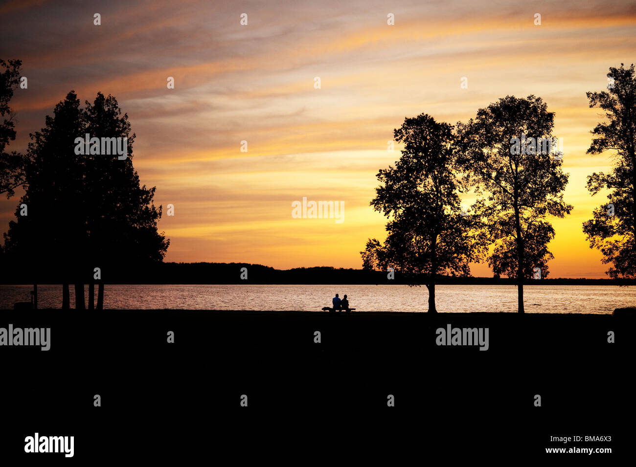 Coppia di anziani e stagliano, seduta su una panchina dal lago al tramonto Foto Stock