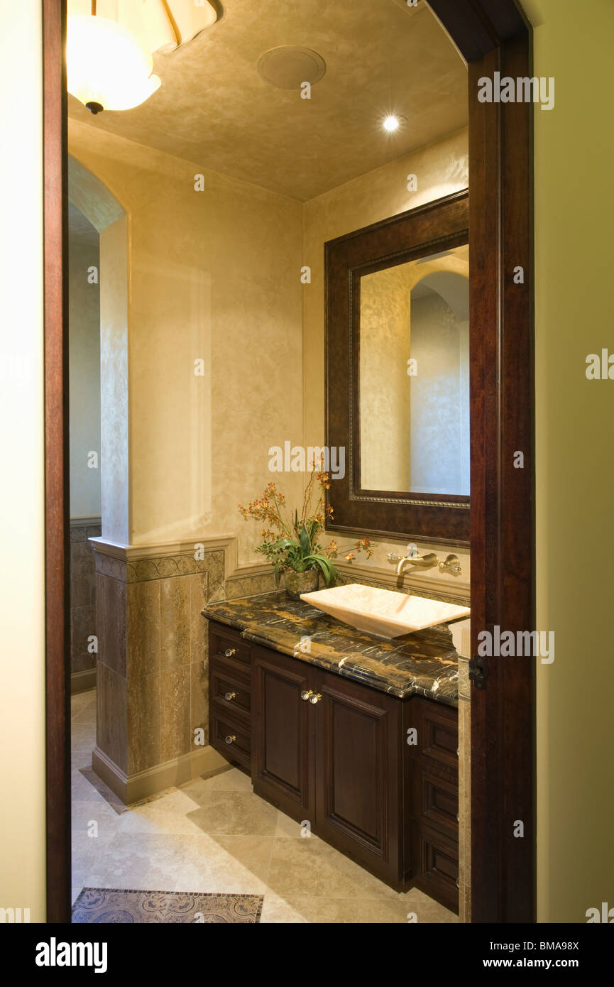 Vista attraverso la porta di legno scuro Bagno con specchio in pelle telaio Foto Stock