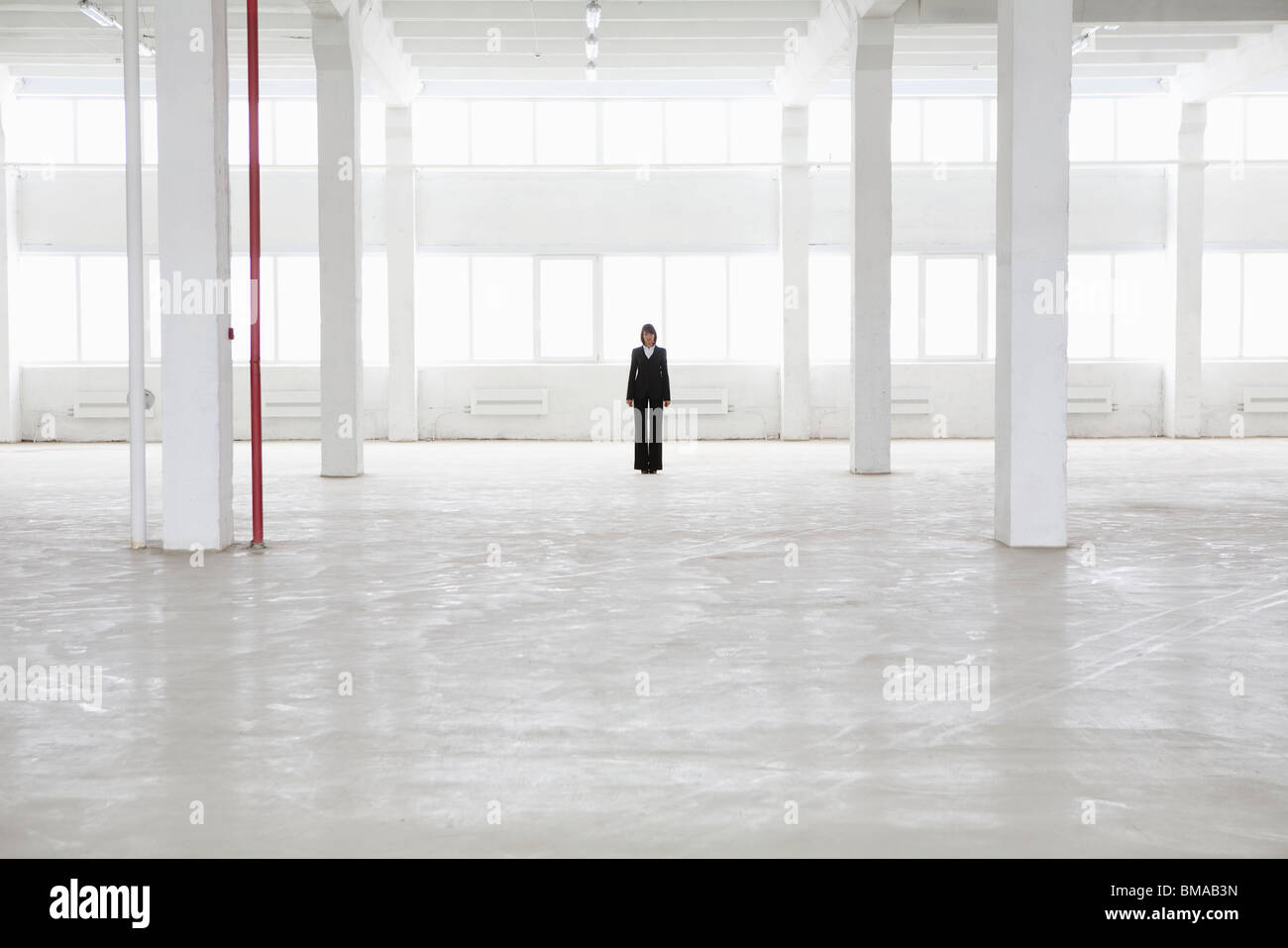 Donna distante sorge in magazzino vuoto Foto Stock