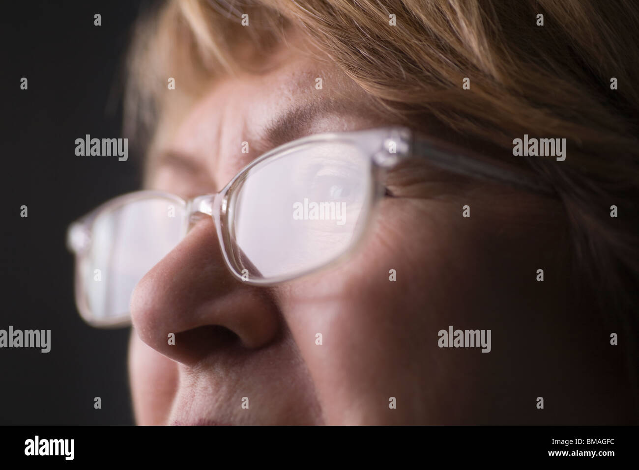 Donna matura con luce riflettendo su gli occhiali da lettura Foto Stock