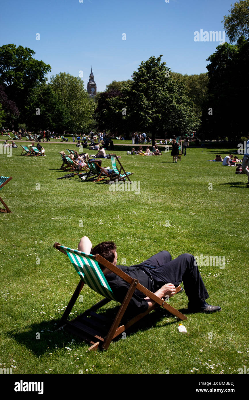 Persone sdraiati sull'erba e seduti sulle sedie a sdraio al sole presso il St James Park, Londra centrale. Foto Stock