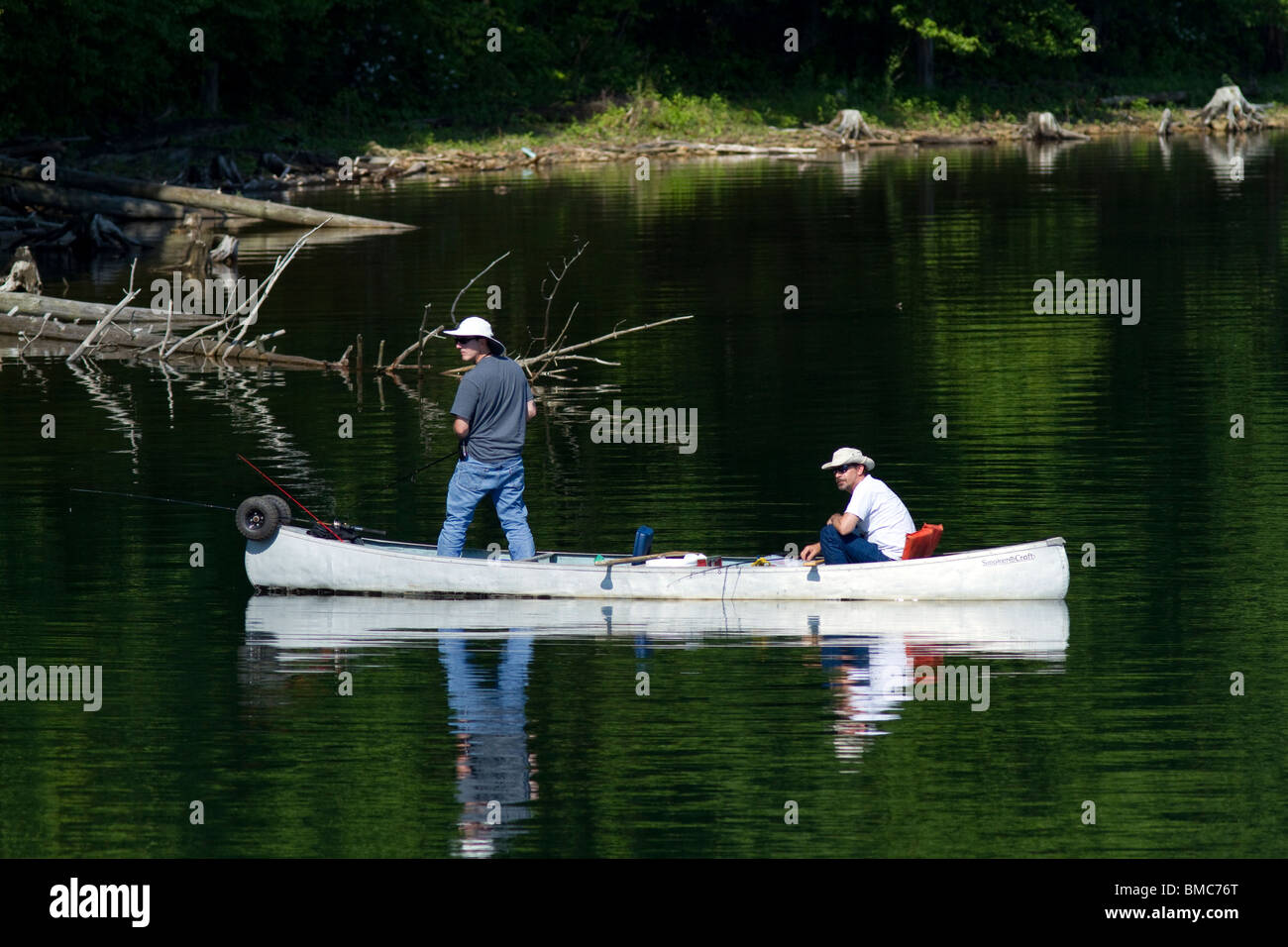 Due uomini a bordo di una canoa pesca lungo la sponda di un lago uno è in piedi. Foto Stock