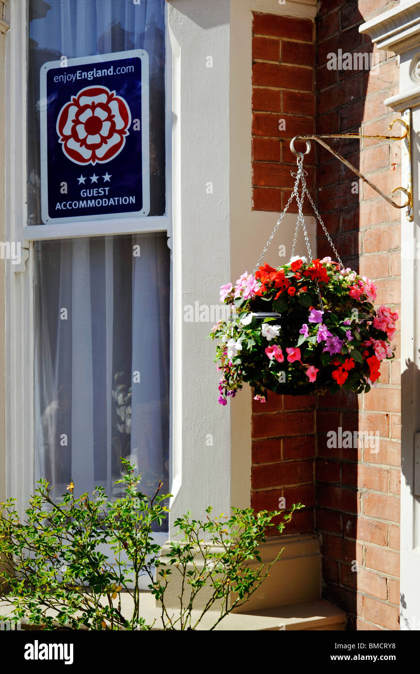 Appendere cesto di fiori e un Enjoy England cartello turistico nella finestra al di fuori di un mare guest house Foto Stock