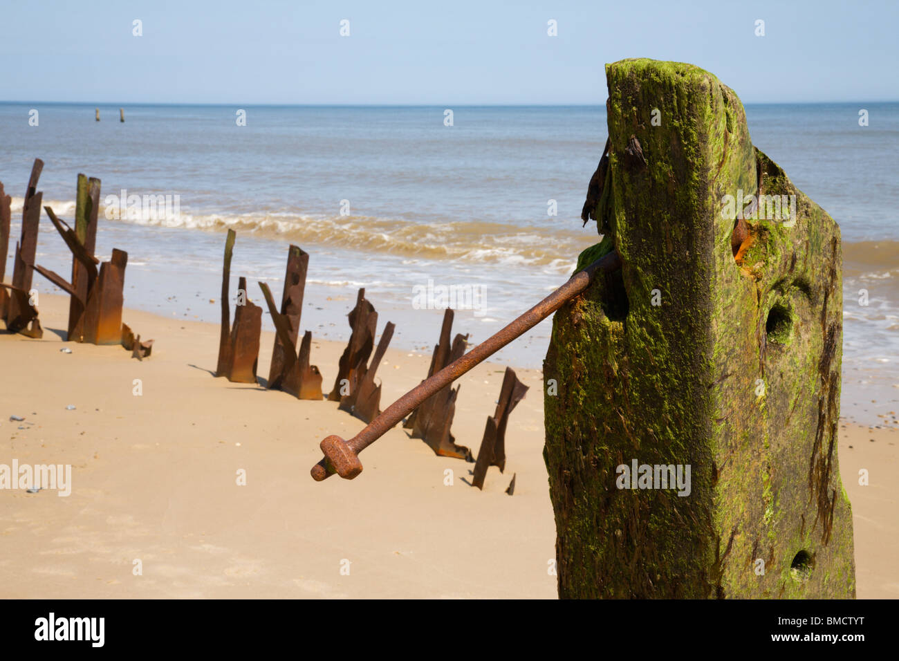 Montanti in legno e ritorto metallo arrugginito lungo Happisburgh seashore, Norfolk. Foto Stock