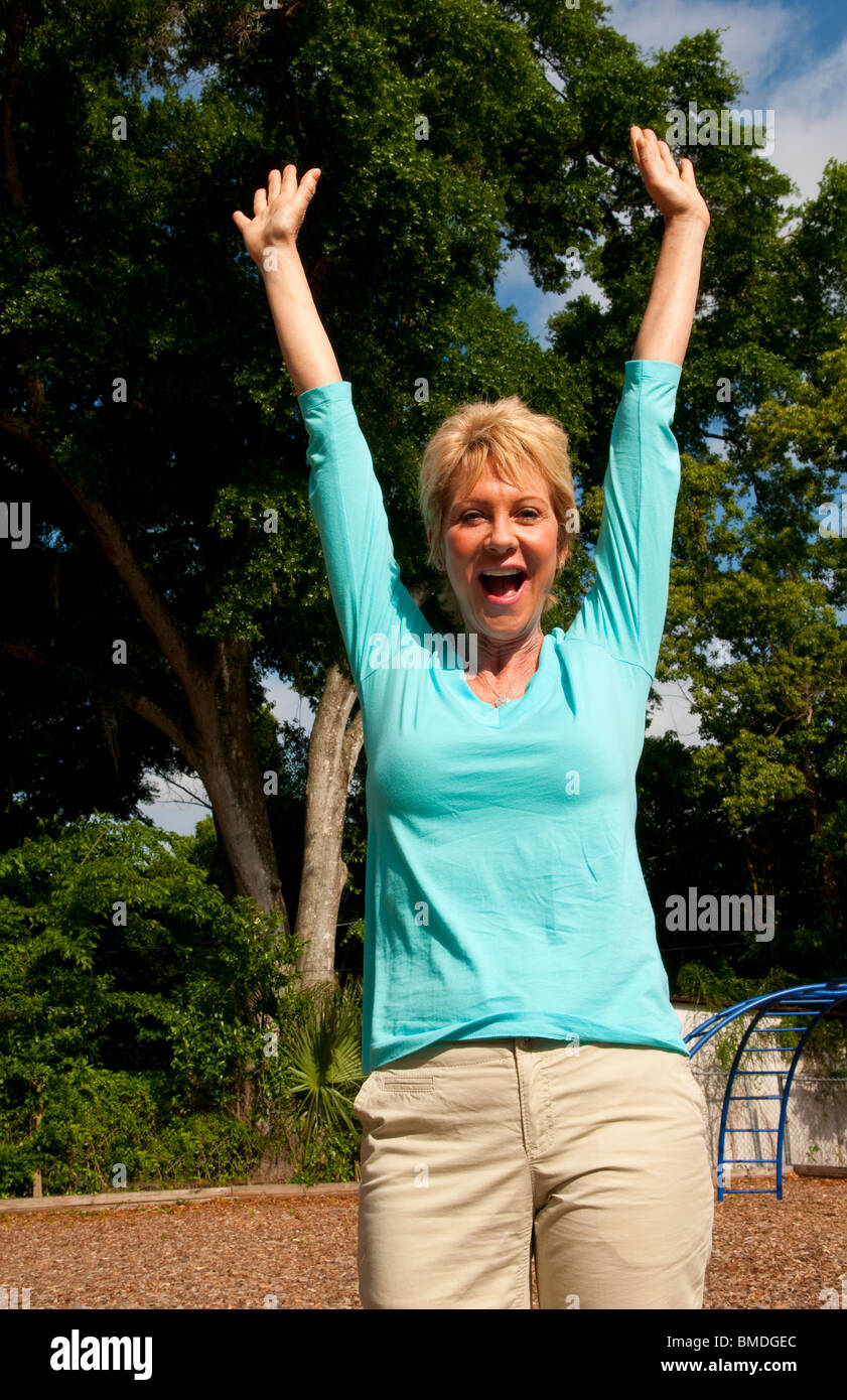 Donna nella sua 60s celebrare con gioia la vita nel parco all'aperto sani Foto Stock