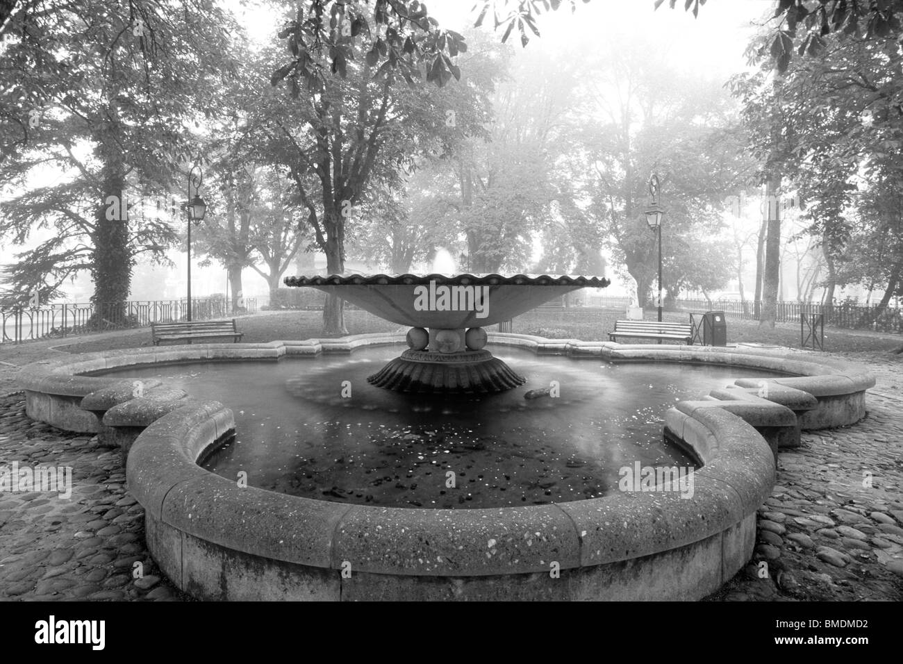 Una foto in bianco e nero di un giardino con una grande fontana in una nebbiosa mattina Foto Stock