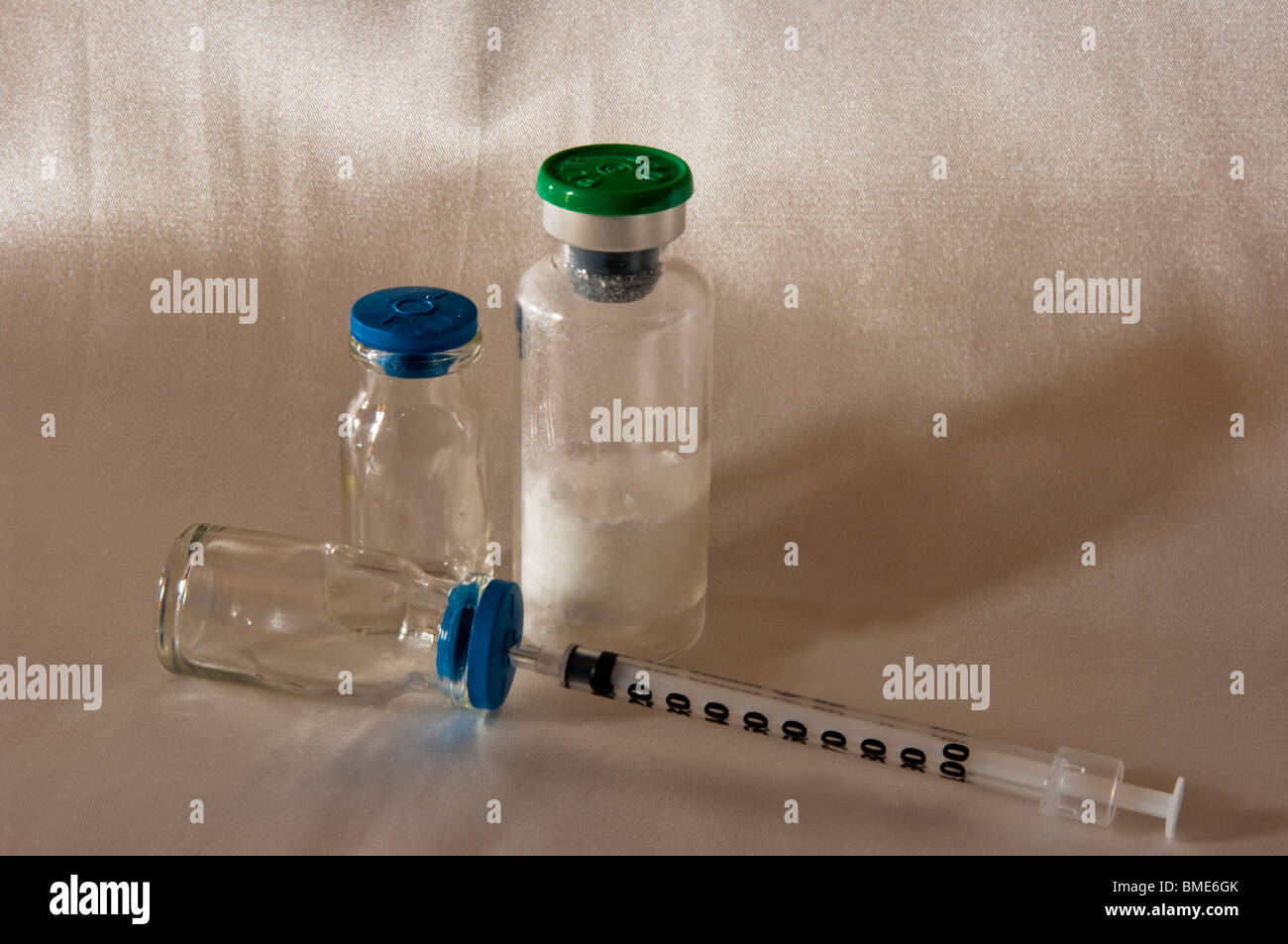 Close up di flaconi vitrei di farmaci iniettivi e di una siringa da insulina che con l'fa ne penetra il tappo colorato in blu Foto Stock