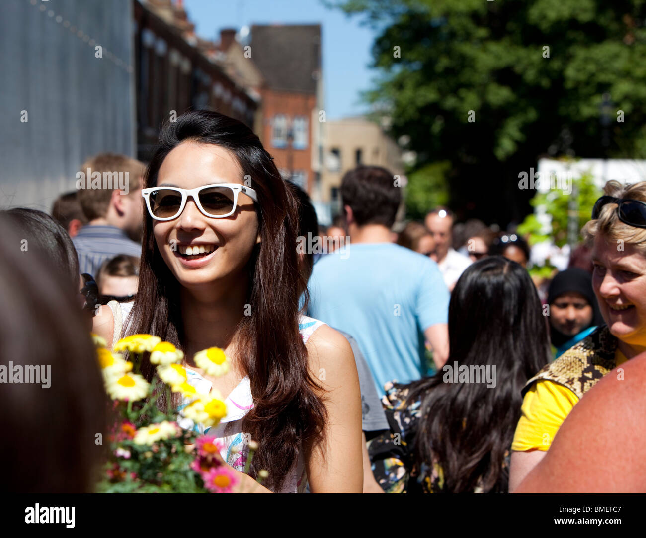 Ritratto di una bella giovane donna sorridente che indossa occhiali da sole al mercato di Sunday Columbia Road, Londra, Inghilterra, Regno Unito Foto Stock