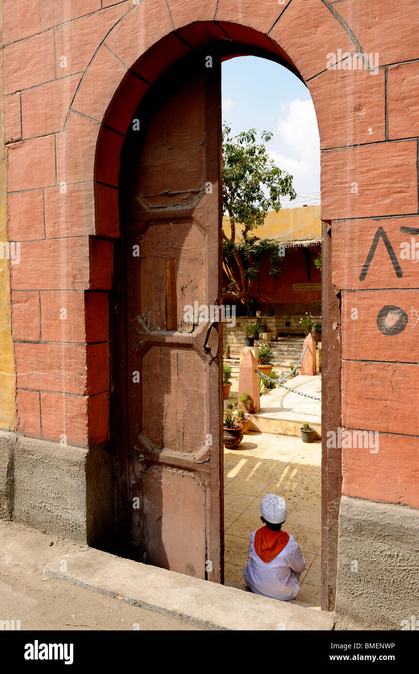 Ragazzo seduto all'ingresso a casa sua nel sud di cimiteri, Il Cairo è la Città dei Morti Foto Stock