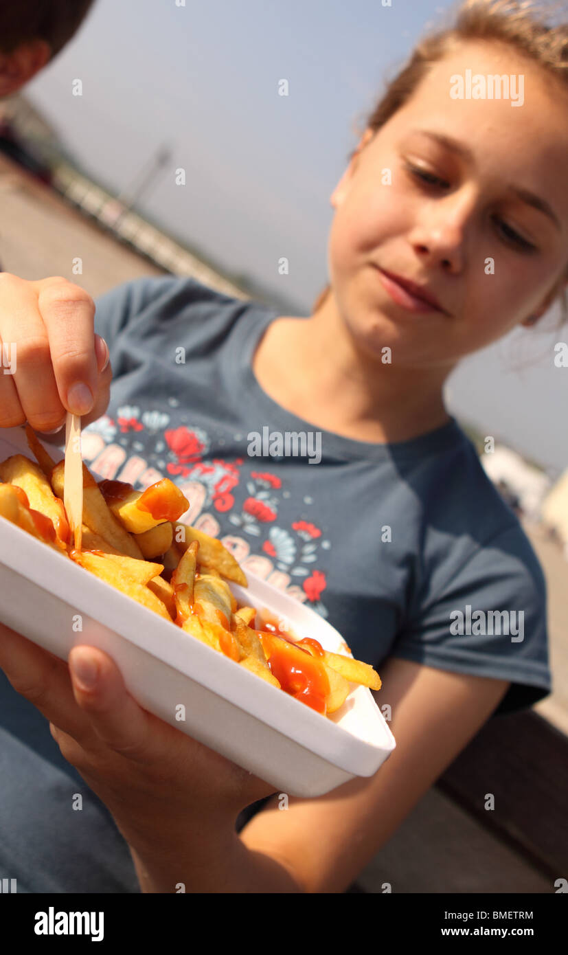 Ragazza adolescente di mangiare una porzione di chip da un vassoio di plastica con forma di legno all'aperto Foto Stock