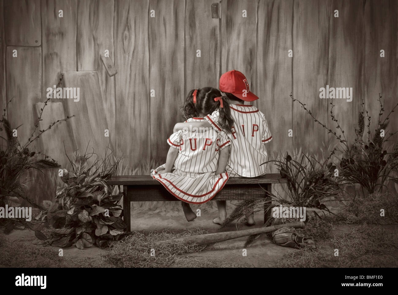Un ragazzo e una ragazza seduta su una panchina di adattamento che indossano uniformi di baseball Foto Stock