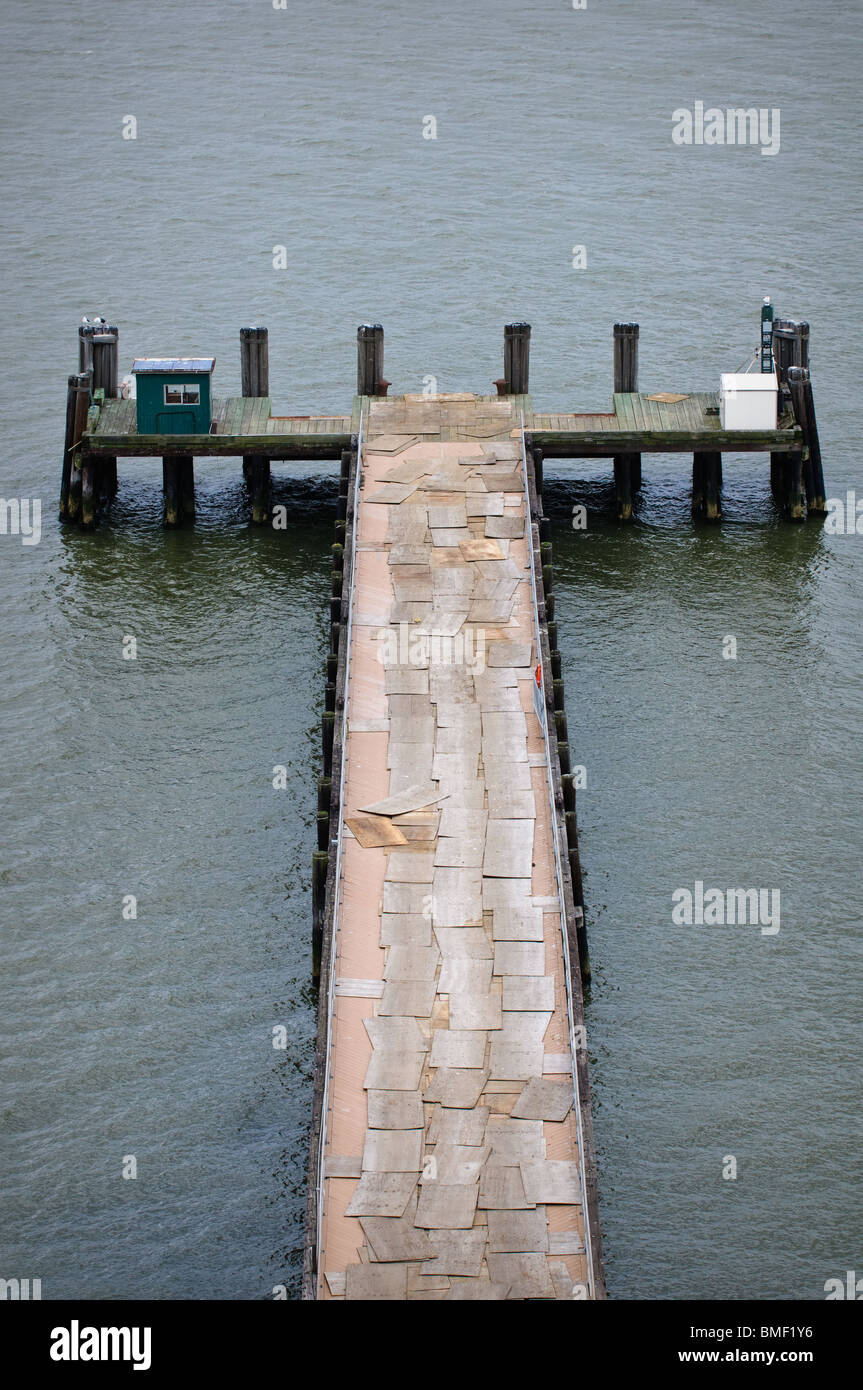 Loose tavole di legno compensato coprire un molo che conduce fuori nell'acqua. Foto Stock