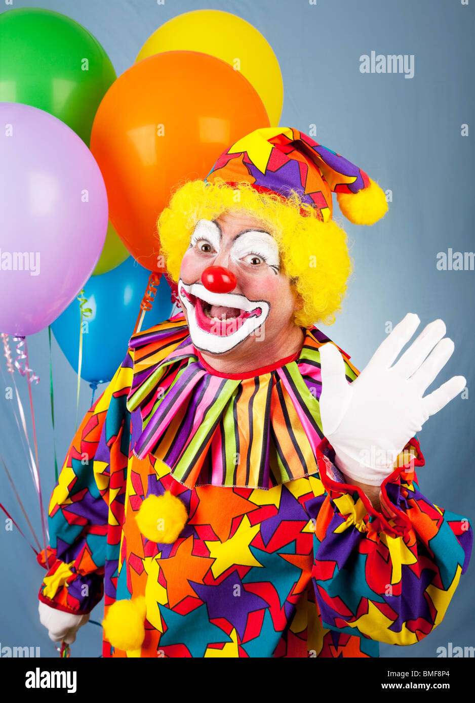 Gentile circus clown tenendo un grappolo di palloncini e salutando. Foto Stock
