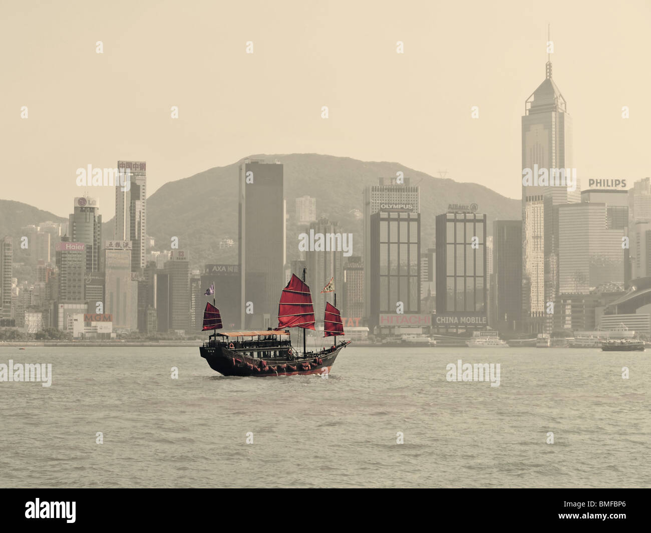 Junk barca che scivola dalla baia di Victoria nella superficie anteriore della Hong Kong skyline di grattacieli, Cina - in seppia e colori rosso Foto Stock