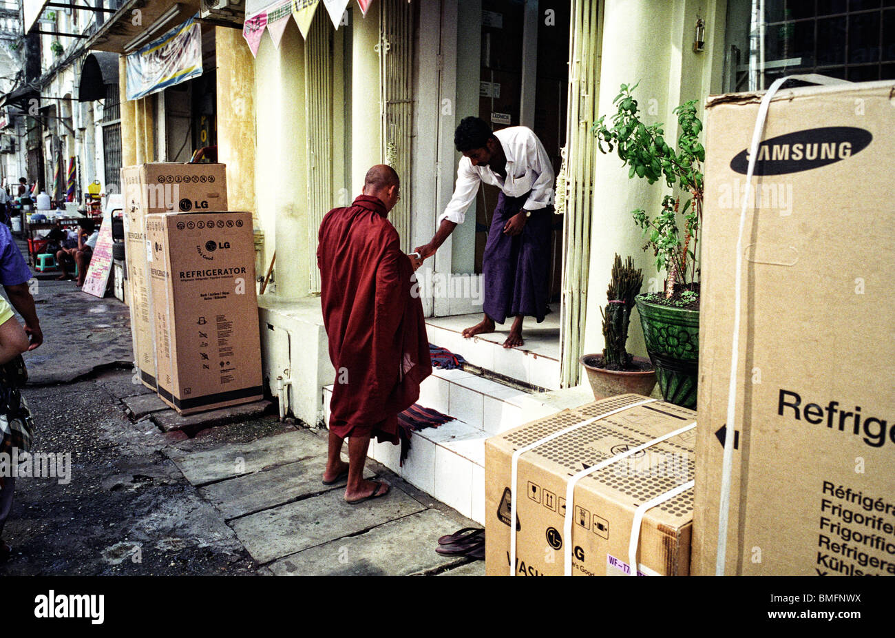 Un monaco riceve l elemosina davanti a un negozio di elettronica a Yangon, Maggio 2010 Foto Stock