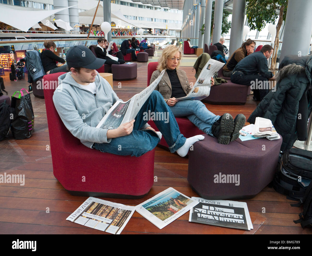 I viaggiatori in aeroporto Stockholm-Arlanda leggere quotidiani mentre aspettano il loro piano. Foto Stock