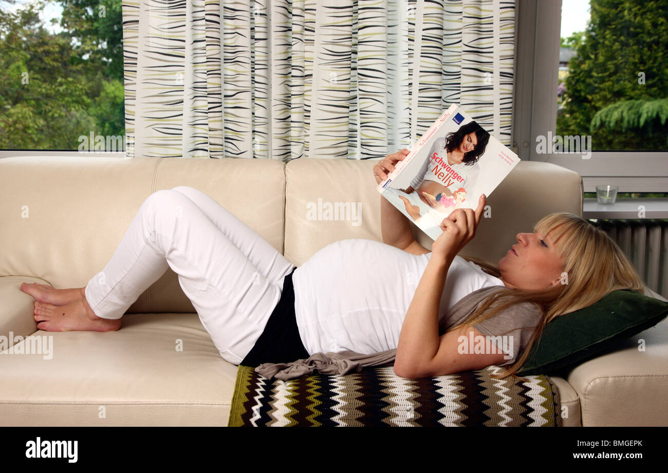 Incinta giovane donna a casa, la lettura di un libro sulla gravidanza. Foto Stock