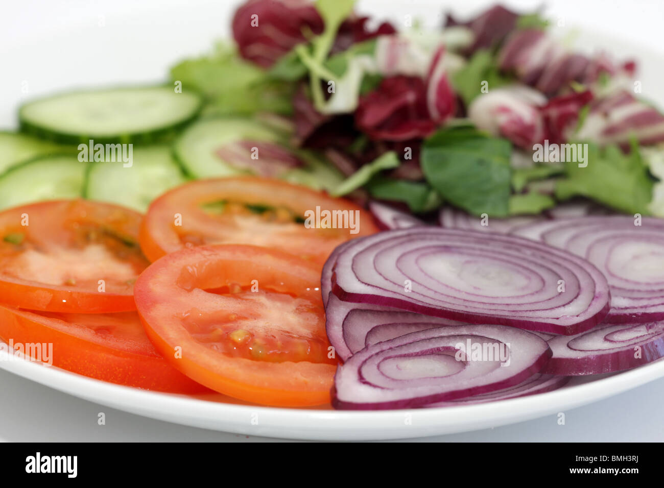 Preparato di fresco vegetariana sana insalata estiva con Pomodori Cetrioli Cipolle rosse e un assortimento di foglie verdi con n. di persone Foto Stock