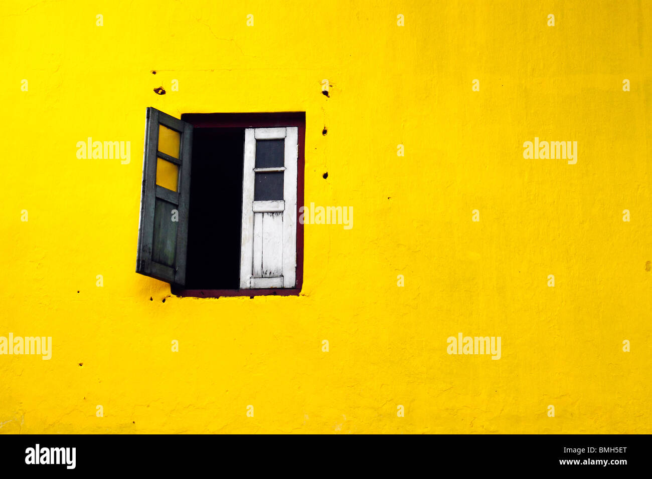 Un solitario vecchio legno finestra su un colorato in giallo parete. Foto Stock