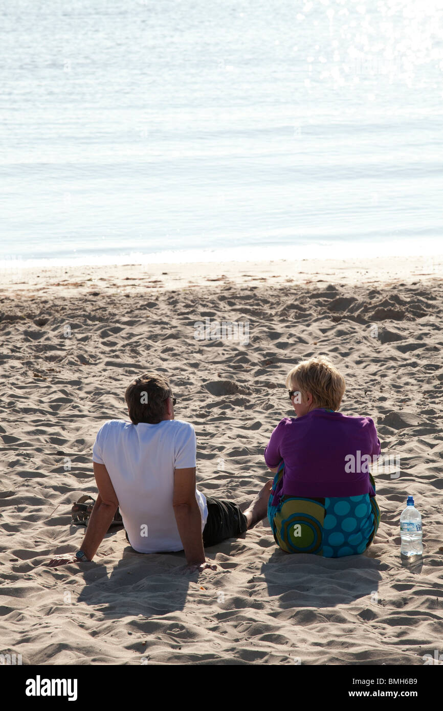 Giovane seduto da solo sulla spiaggia sabbiosa godendo di mattina presto la luce del sole. Foto Stock