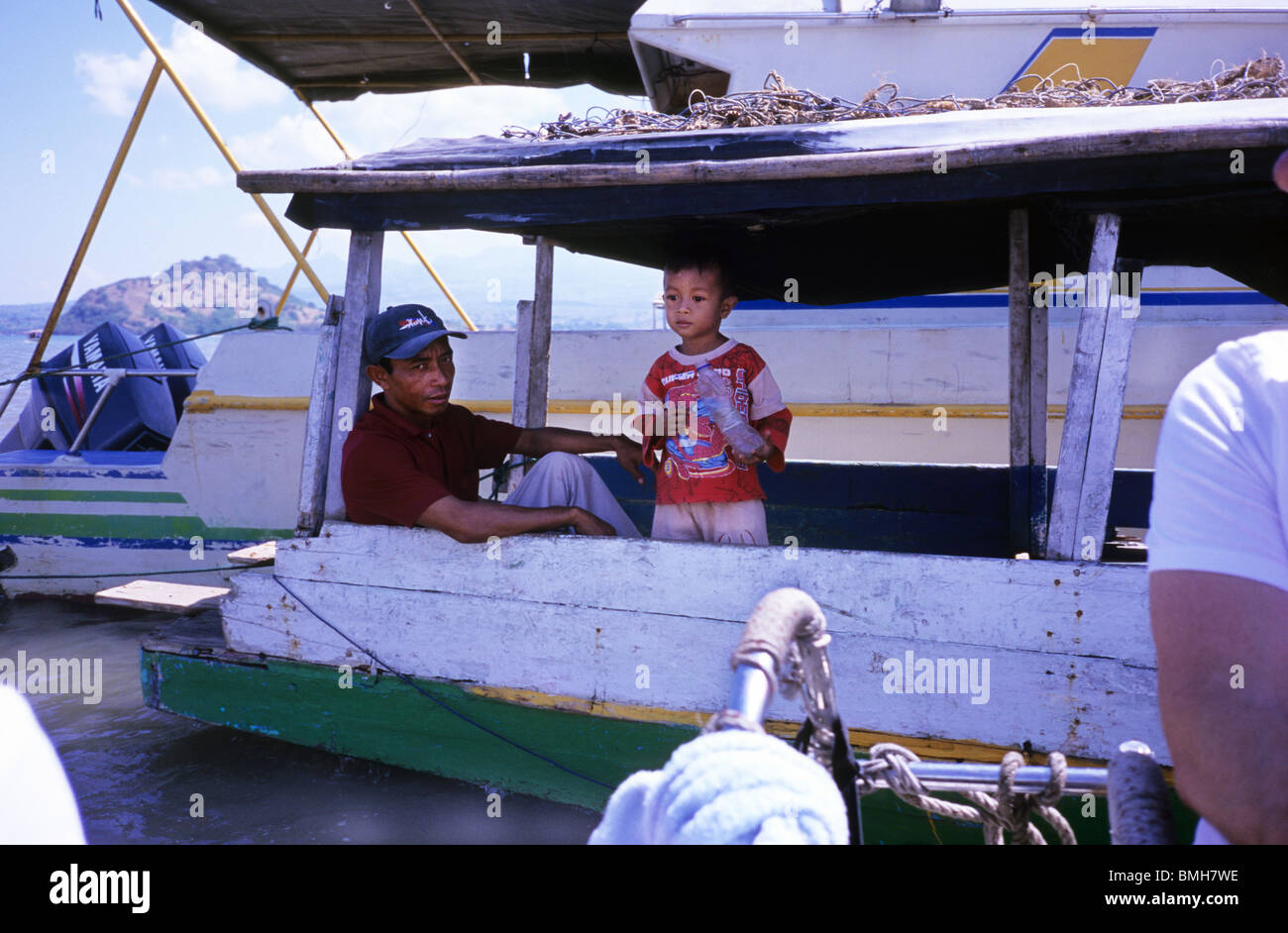 Uomo e ragazzo in attesa su una barca nel porto di Bima. Indonesia. La barca di legno. Piccolo Ragazzo indonesiano con una bottiglia di plastica, guardato da un uomo Foto Stock