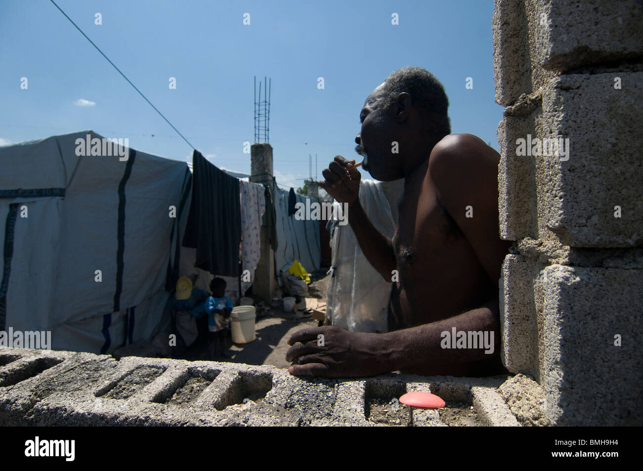 Un terremoto superstite spazzolando i suoi denti accanto a tende di fogli in corrispondenza di una temporanea dimora di fortuna di Port au Prince, Haiti Foto Stock