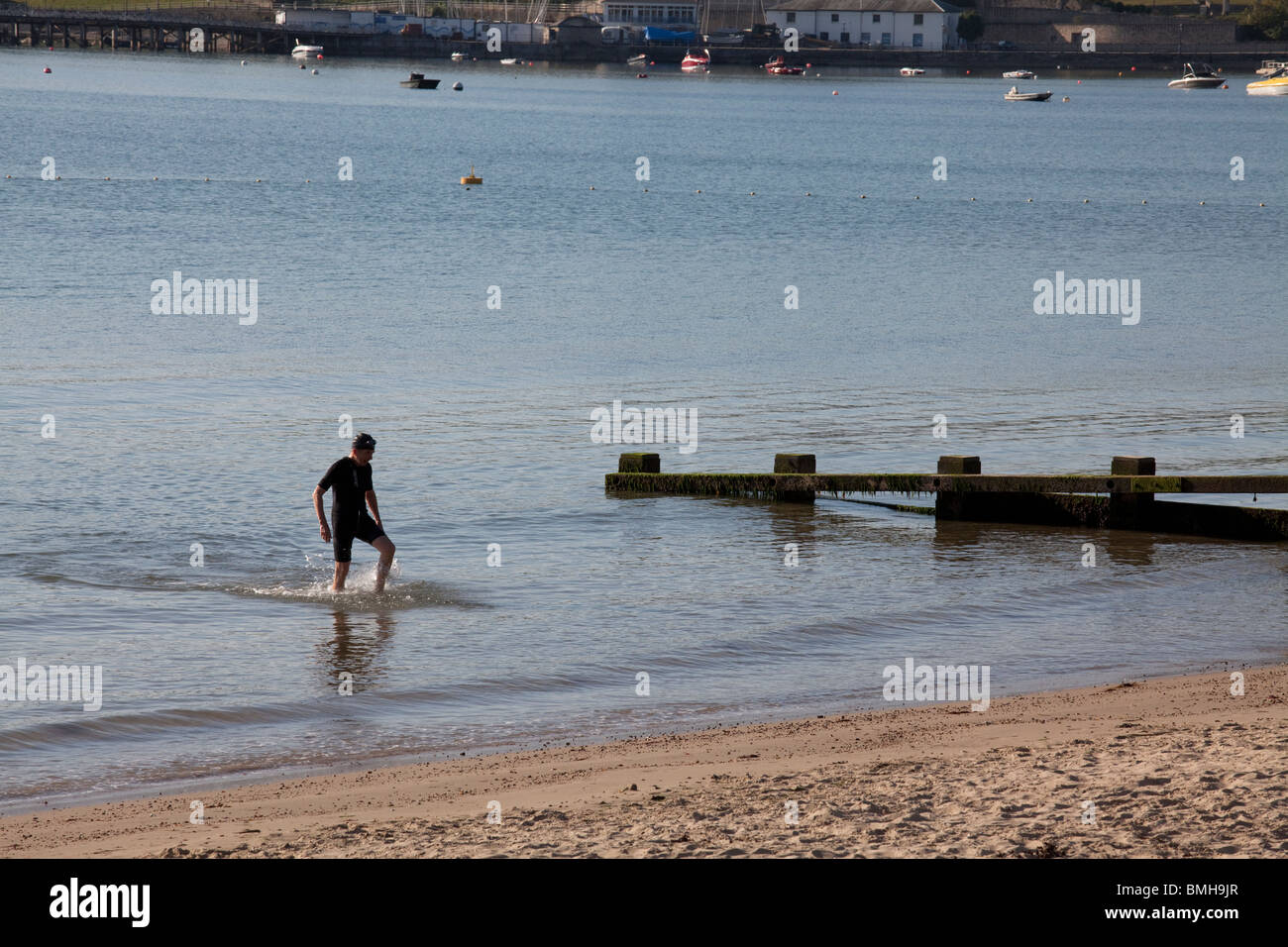 La mattina presto del nuotatore lasciando il mare da un groyne in legno a Swanage Foto Stock