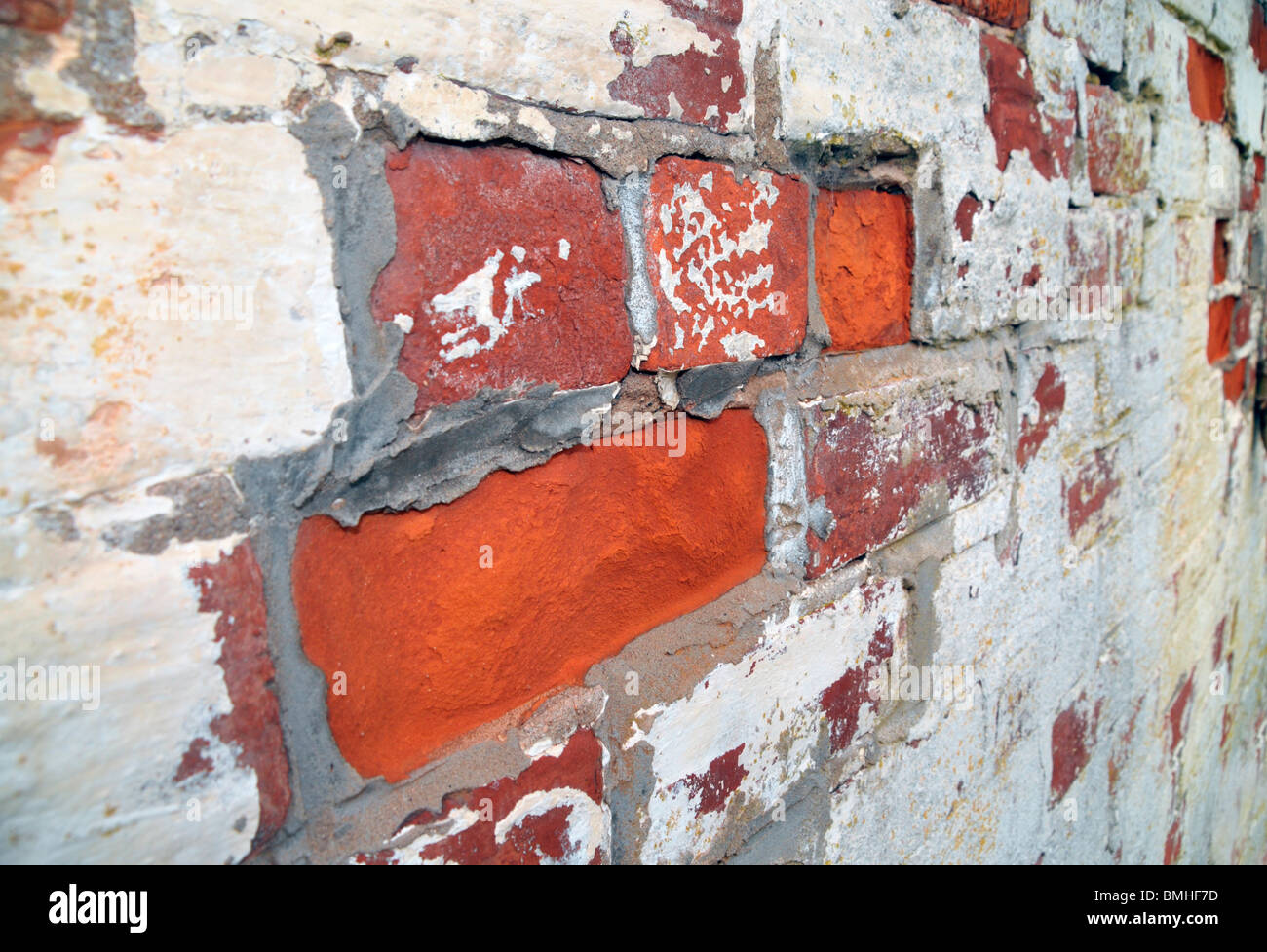 Vista laterale di un peeling parete dipinte di bianco e i suoi mattoni rossi. Foto Stock