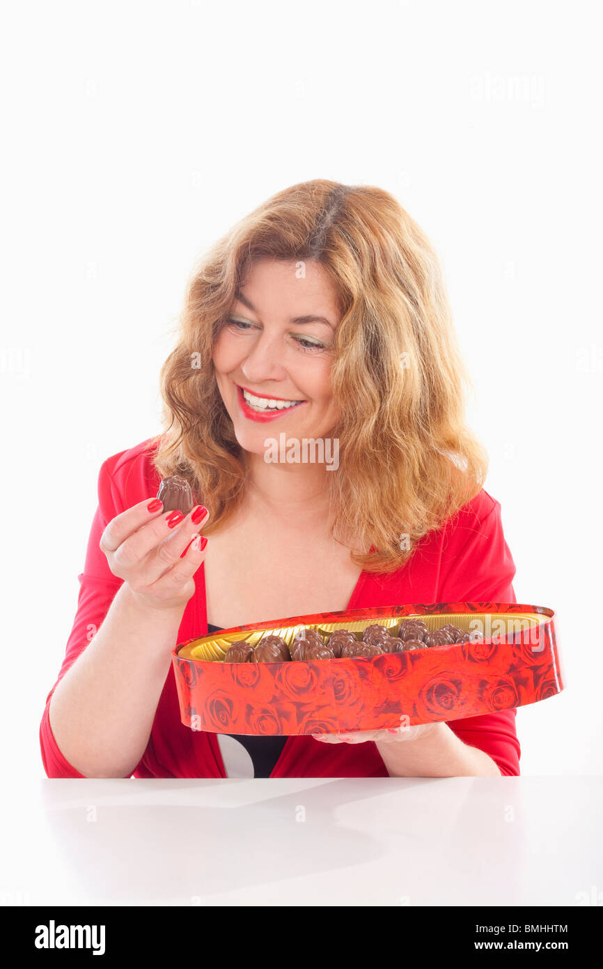 Donna di mezza età in rosso con una scatola di cioccolato - isolato su bianco Foto Stock