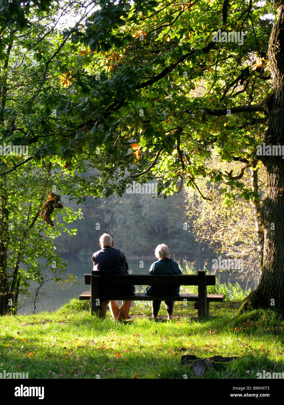 Coppia di anziani seduti su una panchina da un lago rilassante Foto Stock