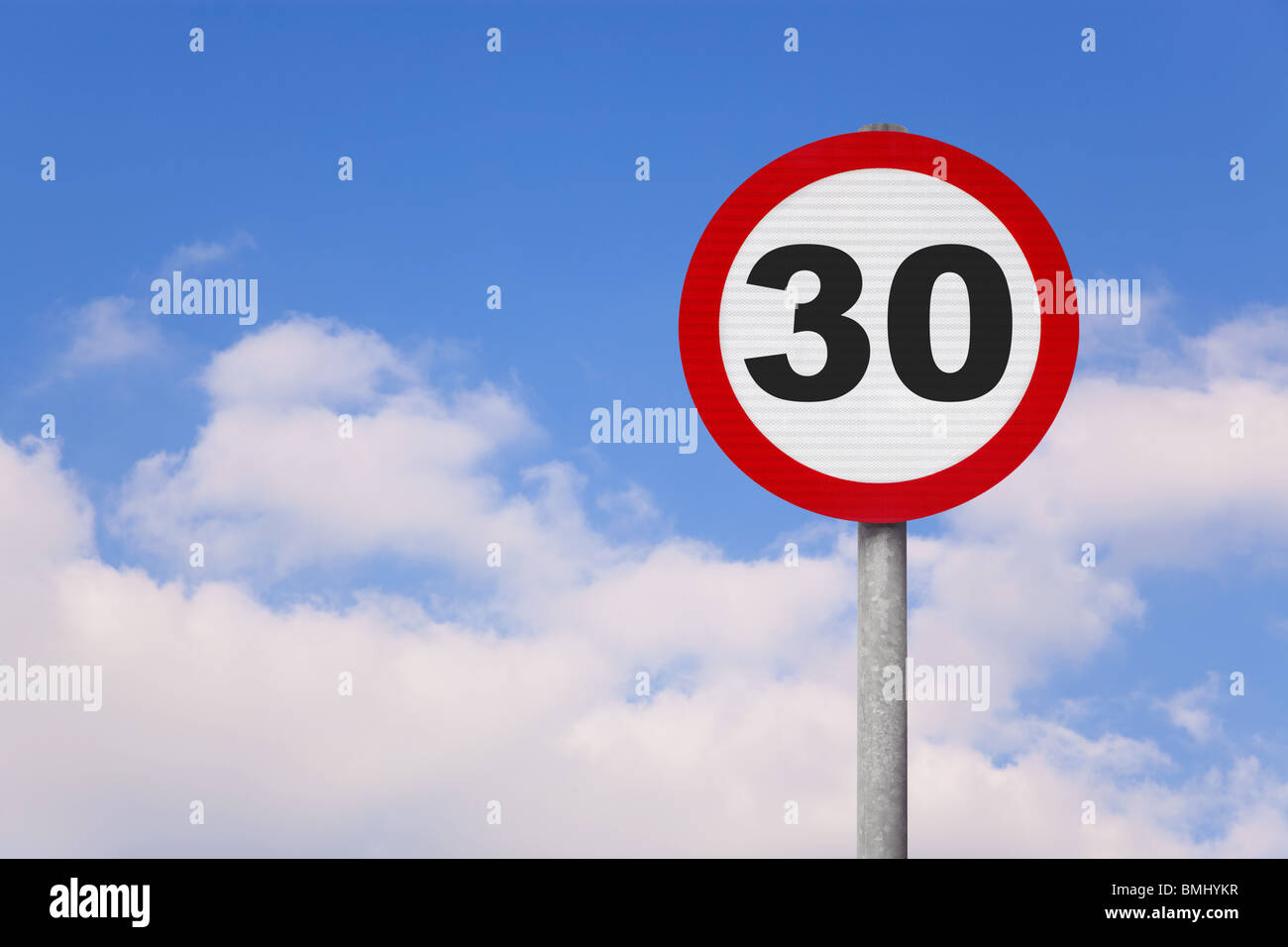 Un round cartello stradale con il numero 30 su di esso contro un blu cielo nuvoloso. Foto Stock