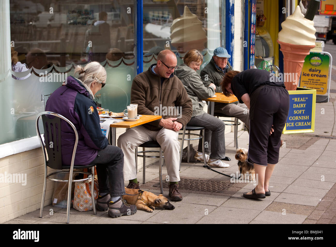 Regno Unito, Inghilterra, Devon, Brixham Harbour, i clienti con cani di bere il caffè al mattino sul marciapiede di tabelle Foto Stock