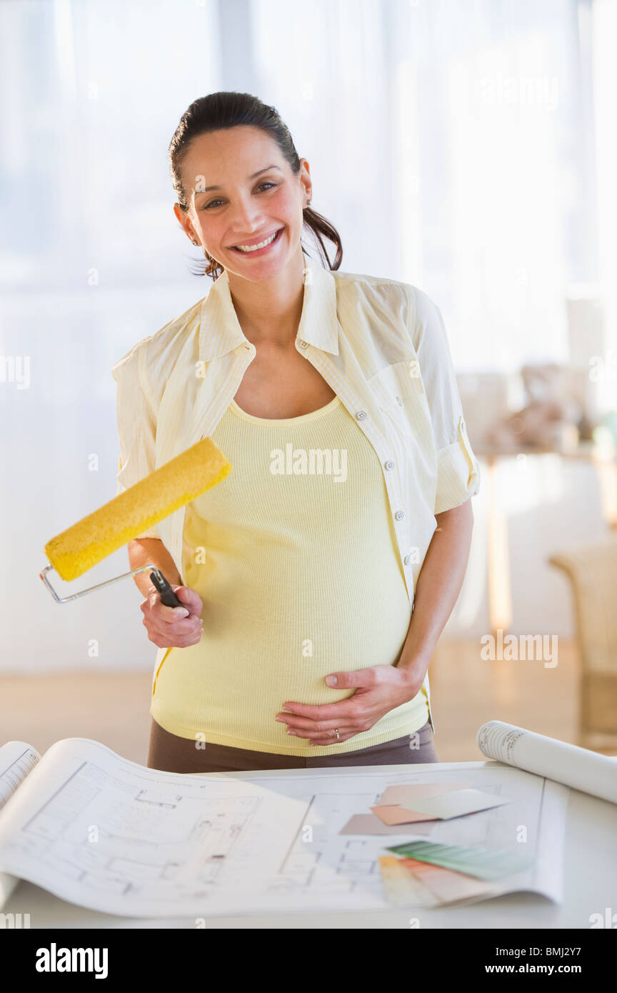 Donna incinta tenendo un rullo di vernice Foto Stock