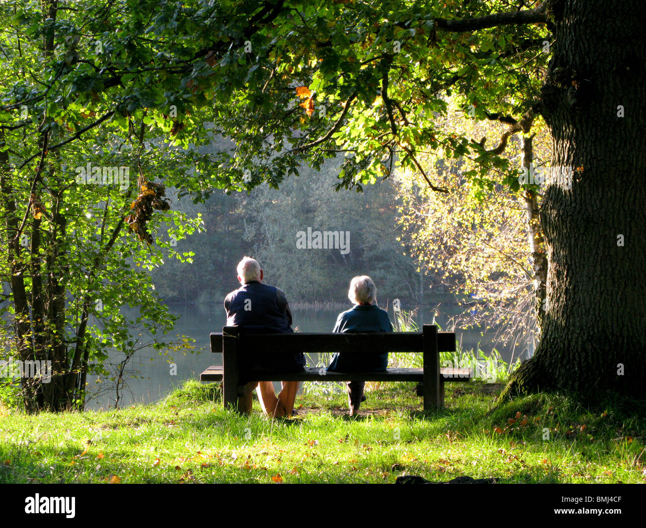 Coppia di anziani seduti su una panchina da un lago rilassante Foto Stock