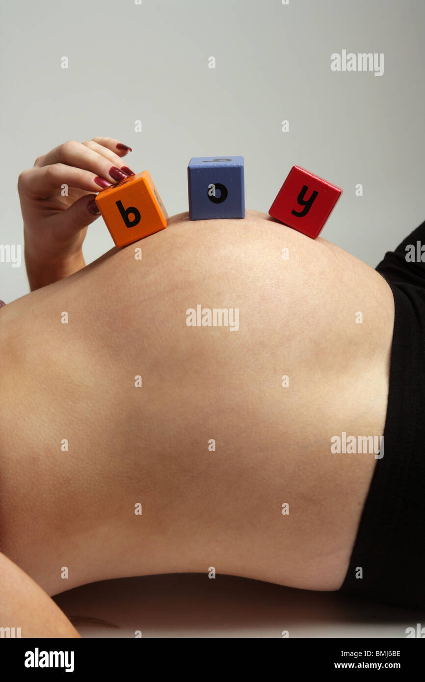 Nove mesi di gravidanza della donna sdraiata sulla schiena con il giocattolo di legno blocchi sul suo ventre ragazzo di ortografia Foto Stock