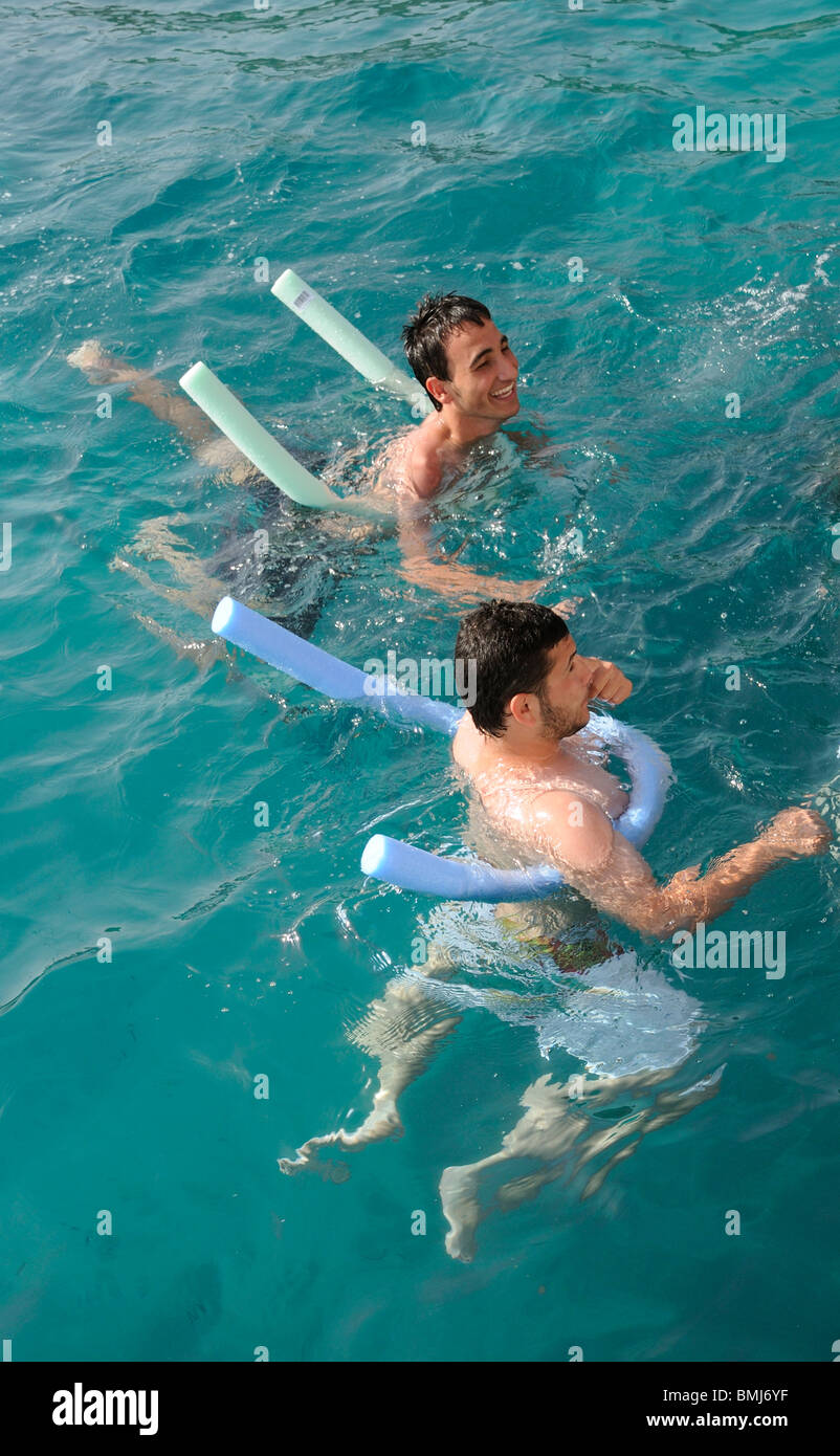 Giovani uomini usando un nuoto tagliatelle come un aiuto di galleggiamento mentre nuotano nel mare Egeo al largo delle coste della Grecia e della Turchia Foto Stock