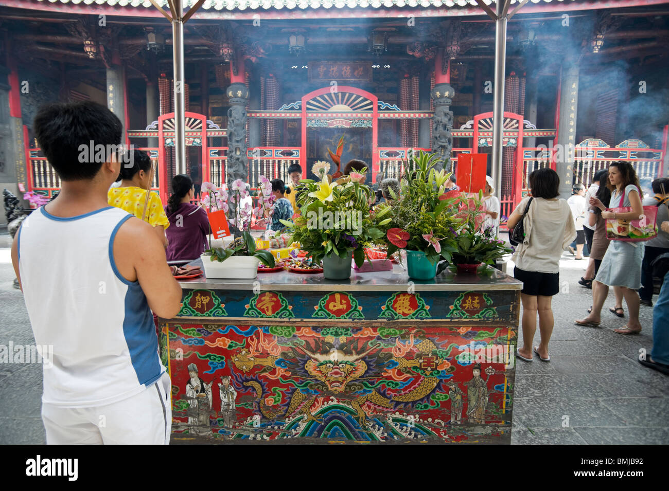 Un visitatore del tempio Longshan in Taipei mantiene le sue mani nella preghiera da un altare dipinto carichi di frutti e fiori. Foto Stock