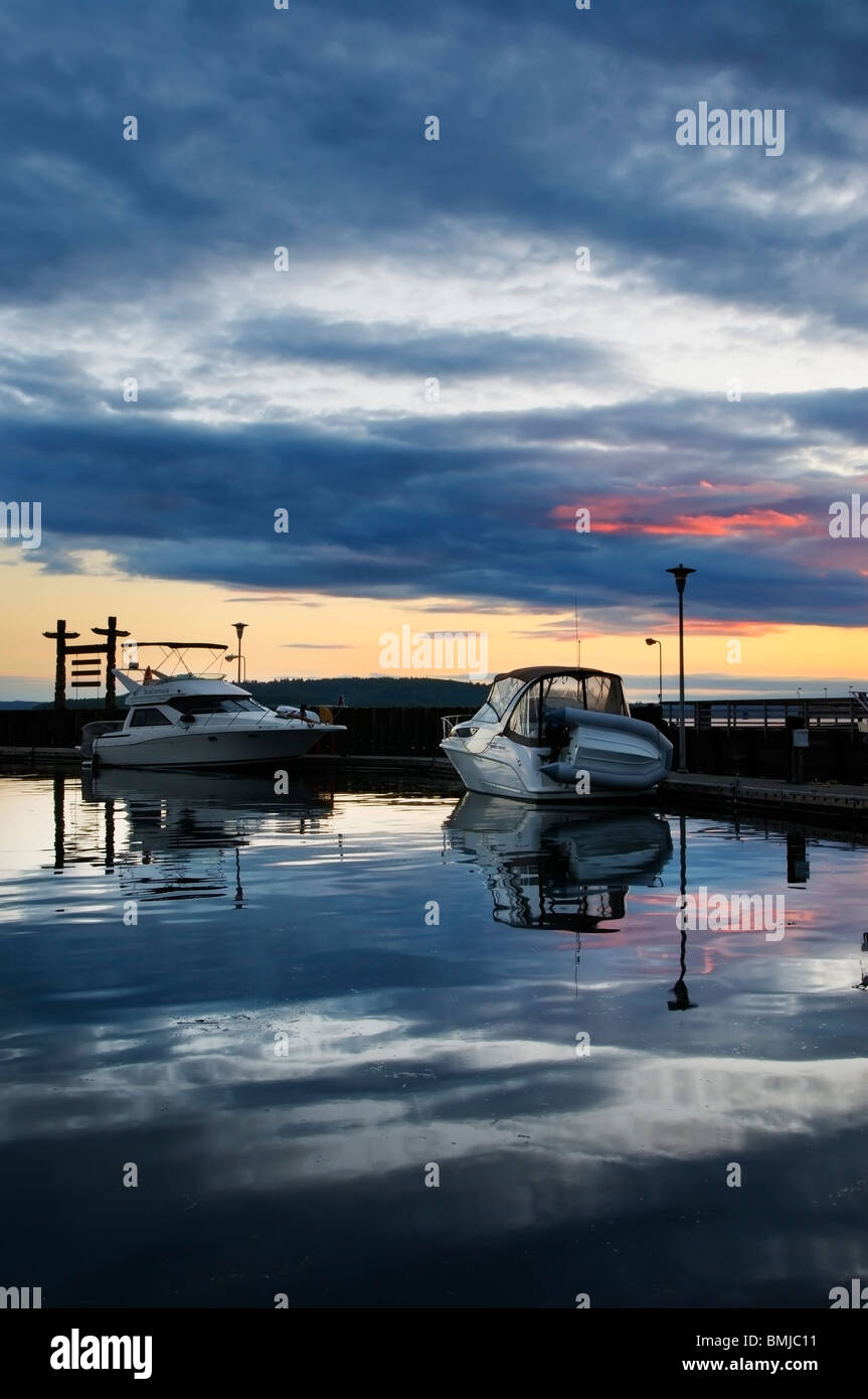 Un bel tramonto e la sua riflessione circondano visitando le barche attraccate al Des Moines Marina valutazione dock sul Puget Sound. Foto Stock