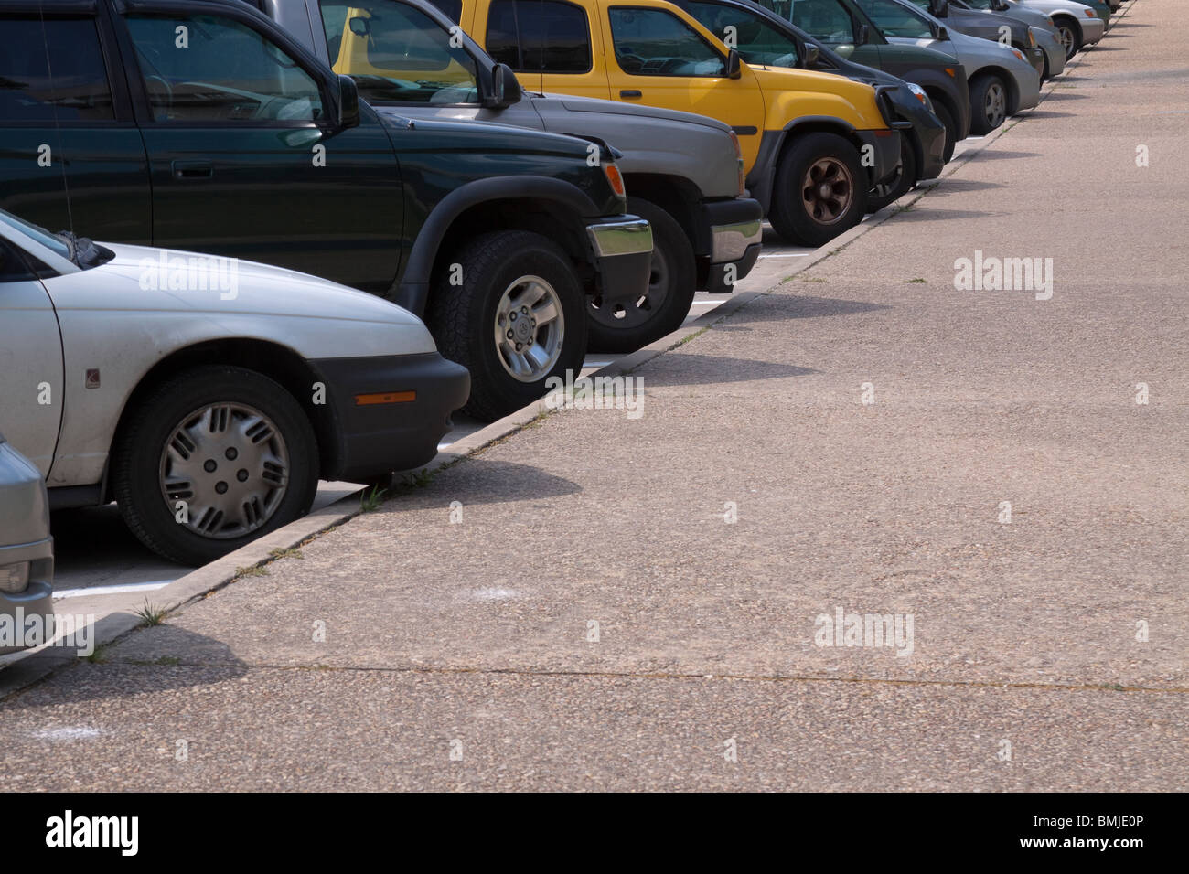 Fila di automobili e suv diagonalmente parcheggiato lungo un marciapiede con un giallo brillante di un SUV nel mezzo. Foto Stock