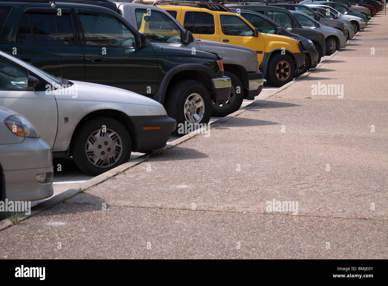 Fila di automobili e suv diagonalmente parcheggiato lungo un marciapiede con un giallo brillante di un SUV nel mezzo. Foto Stock