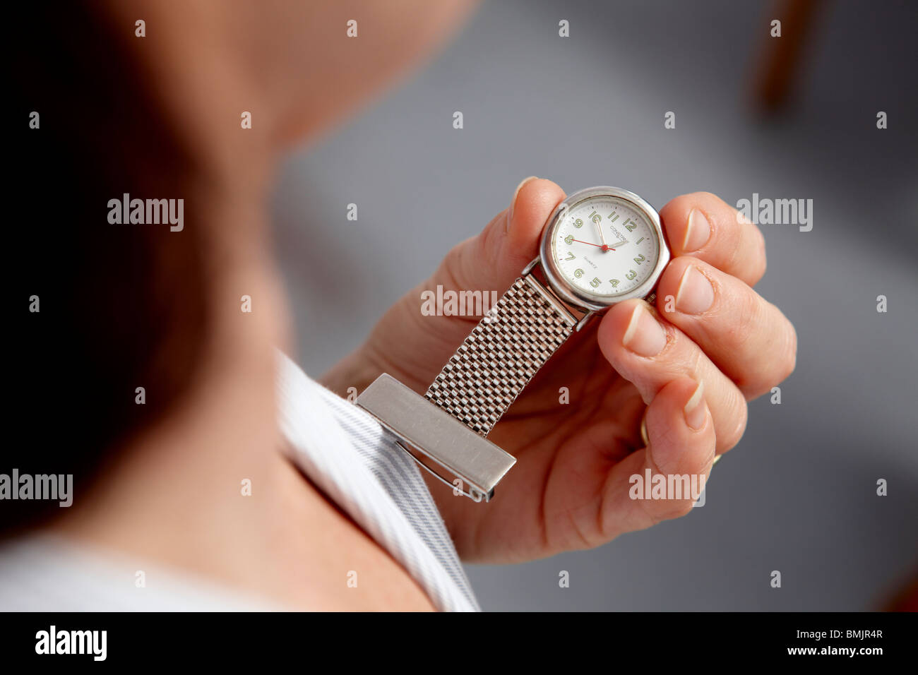 Un infermiere del personale che lavora per il NHS guarda il suo orologio da tasca Foto Stock