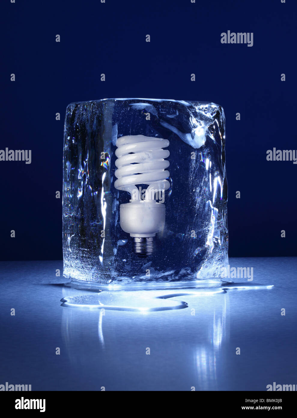 Un blocco congelato di ghiaccio con una compatta lampadina congelate all'interno su una superficie di metallo Foto Stock