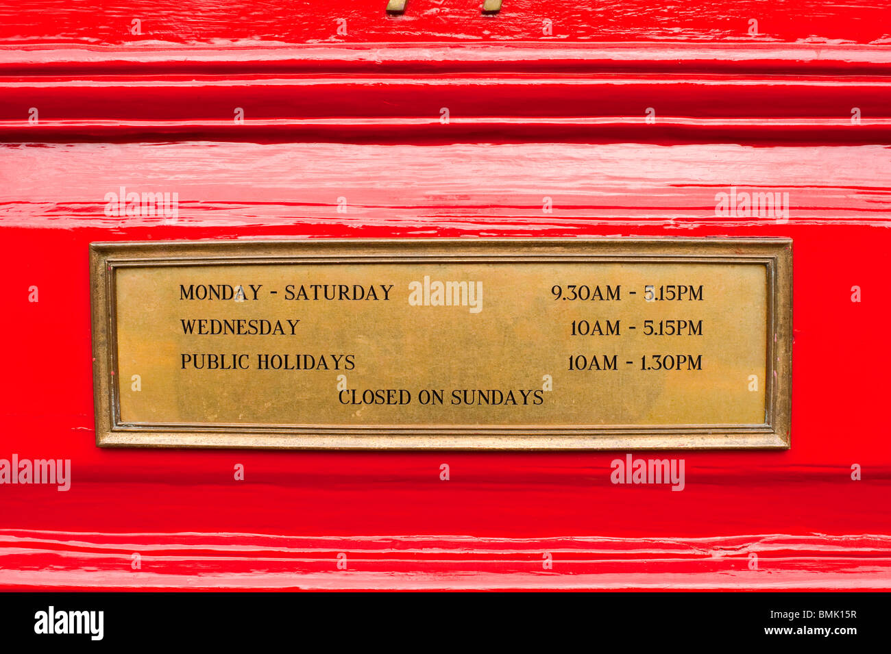 Orari di apertura del segno in ottone sulla porta rossa Foto Stock