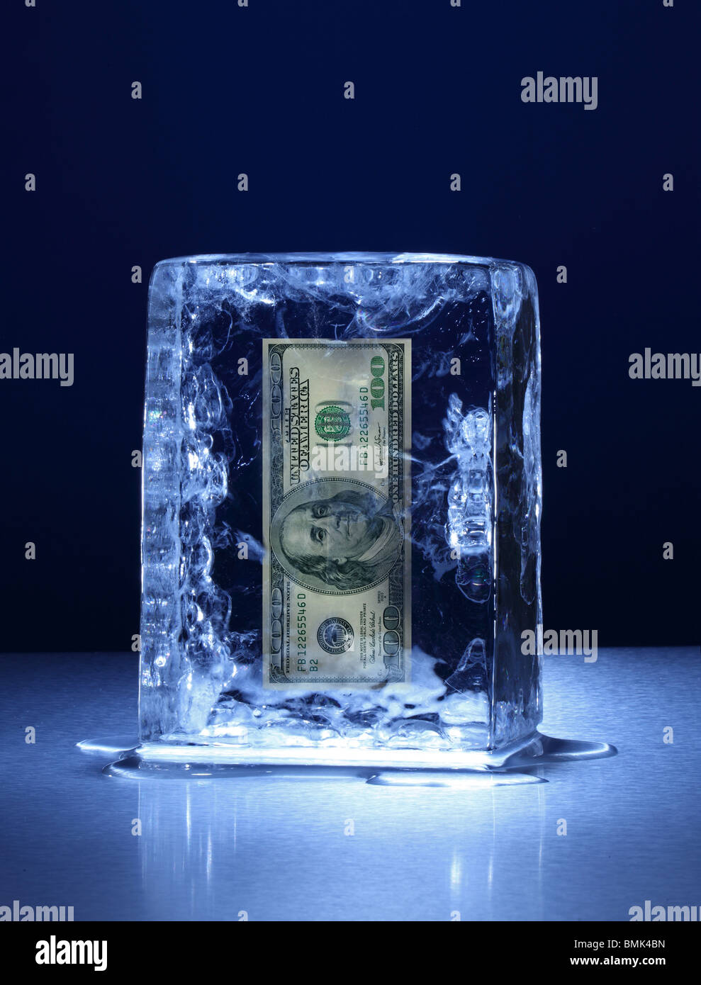 Un blocco congelato di ghiaccio con un 100 US dollar banconota congelate all'interno su una superficie di metallo Foto Stock