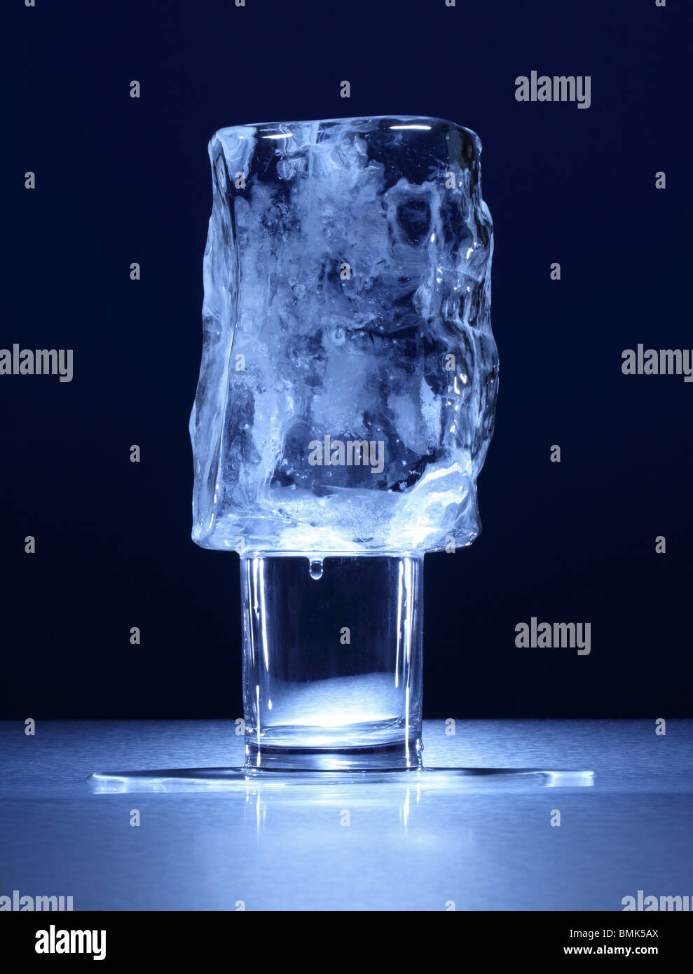 Un vetro trasparente con un piccolo blocco congelato di ghiaccio su una superficie di metallo Foto Stock