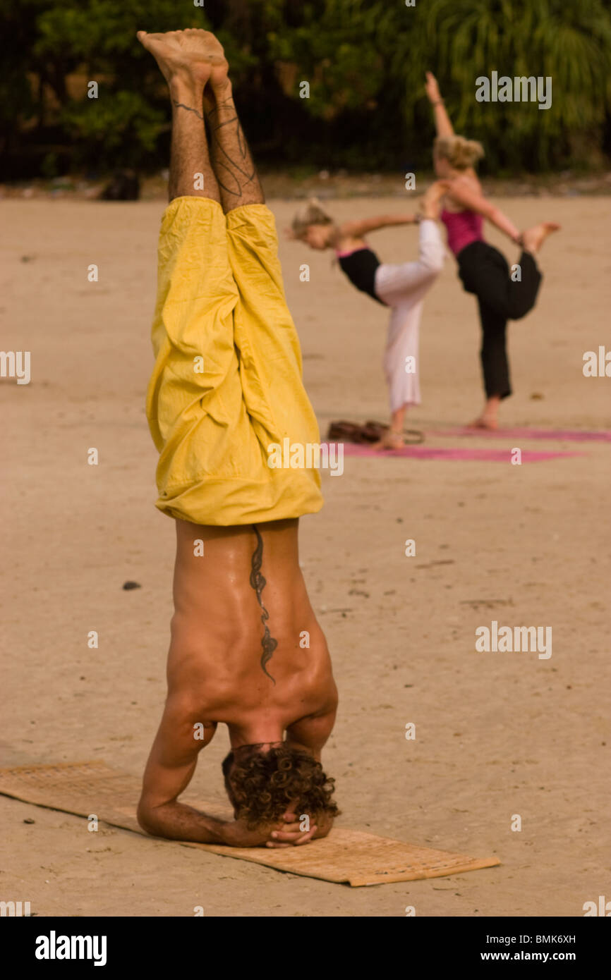 Uomo e due donne facendo un headstand durante la pratica dello yoga sulla spiaggia Kudle, Gorkarna, India Foto Stock