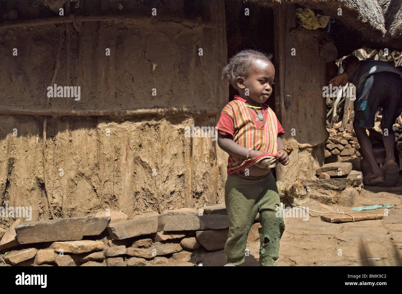 Una piccola ragazza nel verde strappato il sudore pantaloni sorge fuori la sua casa di fango nel villaggio di Gaho, Konso tribù, regione dell'Omo, Etiopia Foto Stock