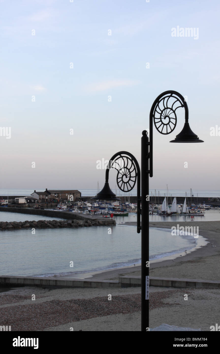 Lyme Regis Spiaggia, Porto e Cobb da Lister giardini al tramonto con spirale fossili street light in primo piano Foto Stock