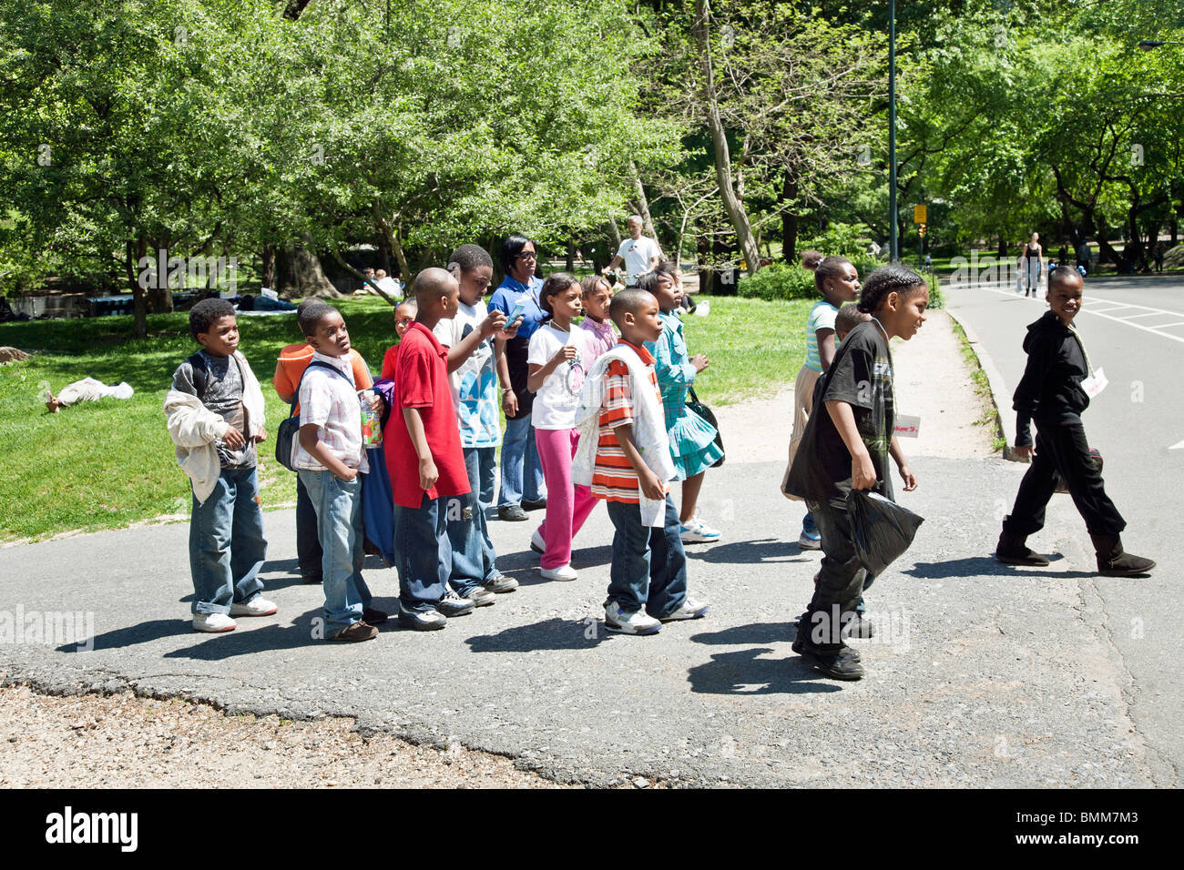 Gruppo vivace nero della scuola elementare i bambini con insegnante & prefetti su una gita scolastica a Central Park sulla splendida giornata di primavera Foto Stock