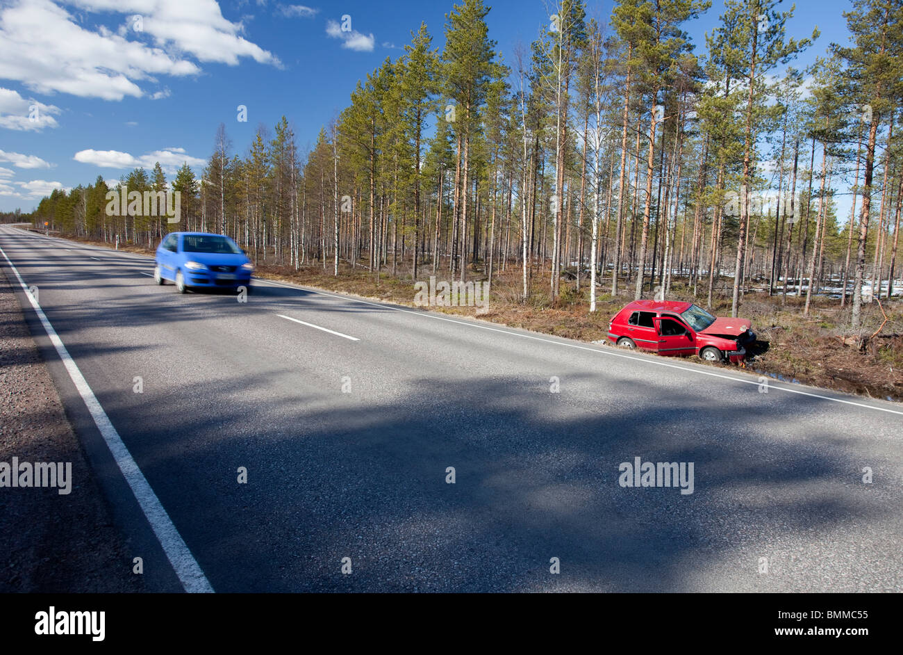 Auto blu che passa da un crash Volkswagen Golf rosso posa a bordo strada fossato, Finlandia Foto Stock